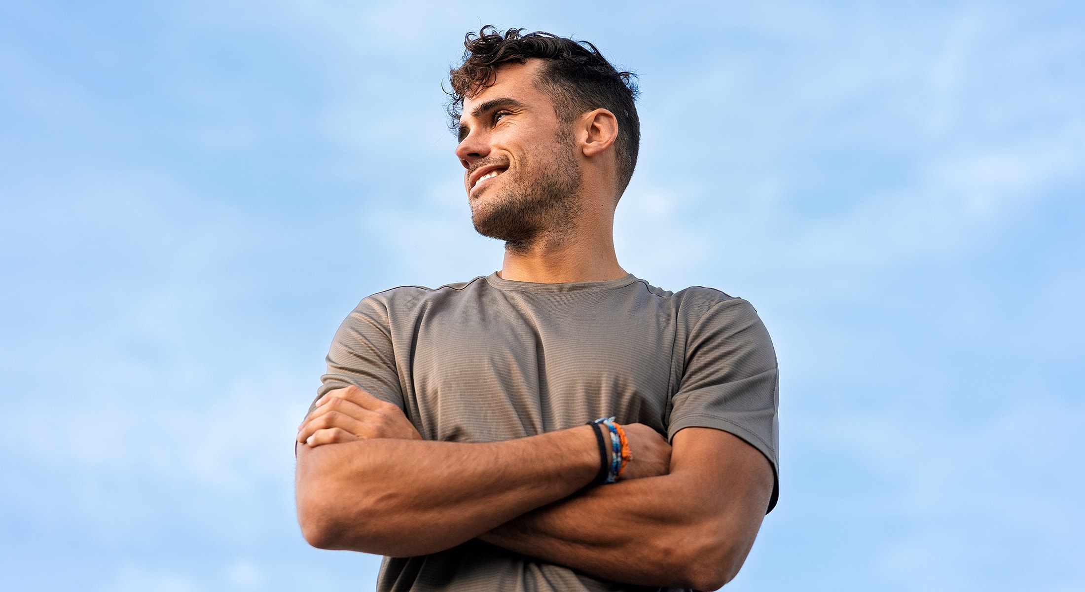 Smiling man with arms crossed against blue sky.